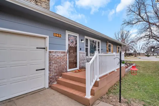 Exterior of a light blue house with a white garage door, brick accents, and a wooden porch with white railings.