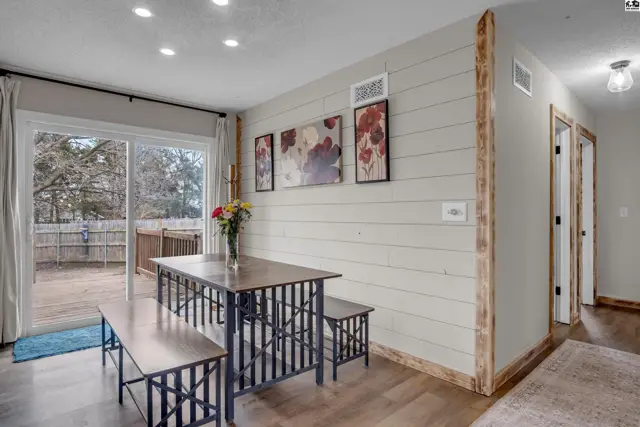 Dining area with shiplap walls, metal-accented table and benches, and sliding glass doors to a deck.