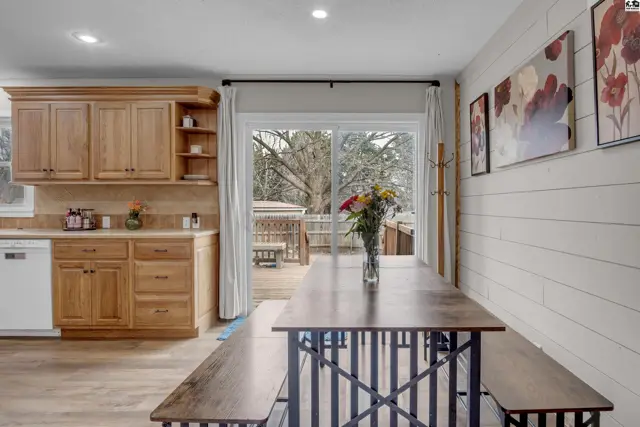 Dining area with wood table and benches, adjacent to kitchen with oak cabinets and sliding glass doors to deck.