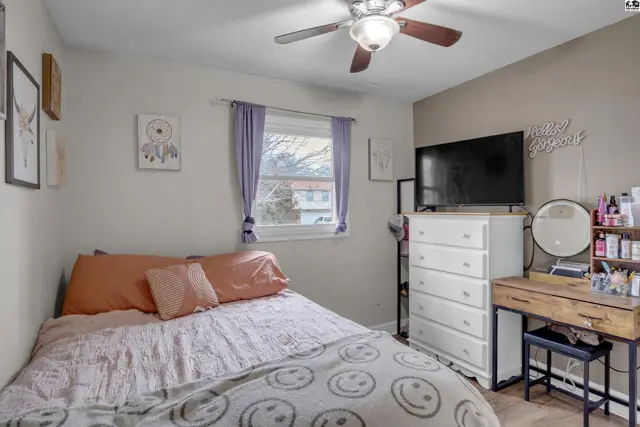 Cozy bedroom with a queen bed, white dresser, vanity, and ceiling fan.