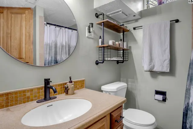 Modern bathroom with a round mirror, wood vanity, tiled backsplash, and industrial pipe shelving.