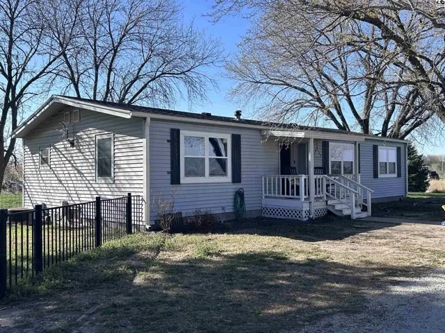 Light blue vinyl-sided manufactured home with a white porch and black metal fence.