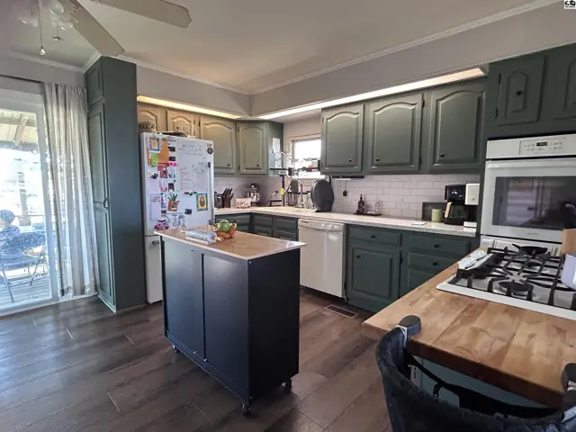 Spacious kitchen with dark green cabinets, white subway tile backsplash, and a butcher block island.