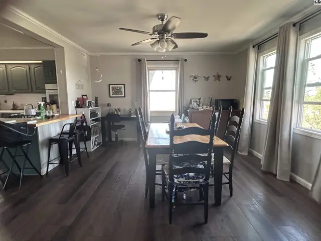 Spacious dining room with dark wood table, black chairs, and large windows, adjacent to a kitchen with gray cabinets.