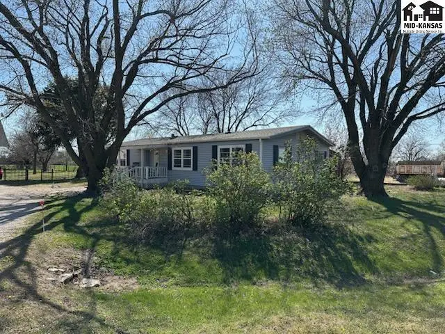 Light blue manufactured home with white trim and shutters sits on a grassy lot shaded by mature trees.