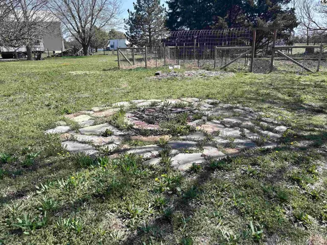 Circular stone fire pit with metal grate sits in a grassy yard with a wooden fence.