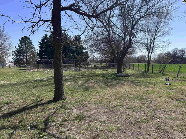 Spacious yard with mature trees, fencing, and a distant view of green fields.