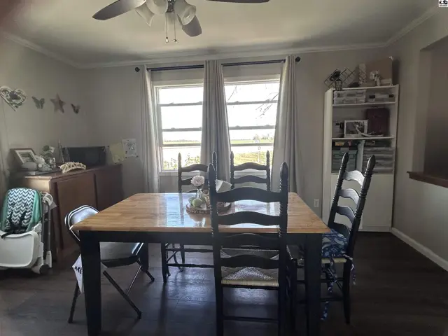 Dining room with a wooden table, dark wood floors, and a large window overlooking a field.