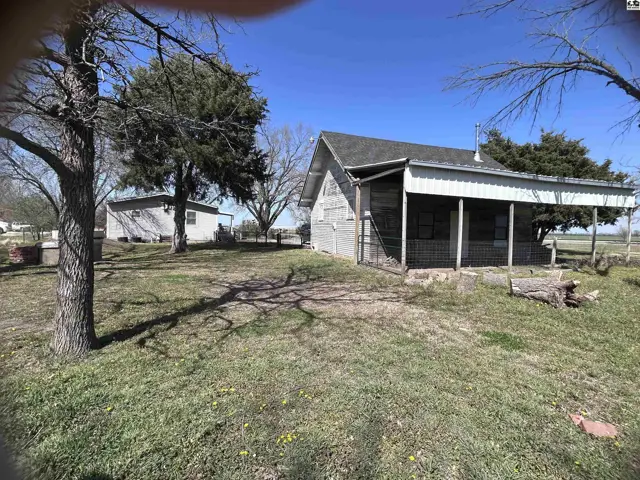 Rustic wooden cabin with a covered porch sits on a grassy lot with mature trees.