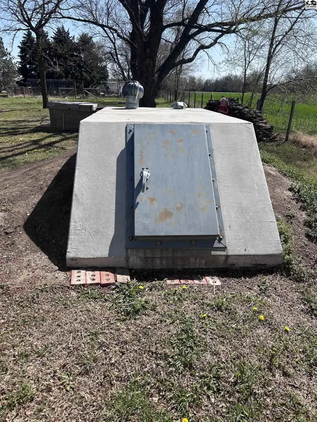 Concrete storm shelter with a metal door and ventilation pipe, set into a grassy embankment.