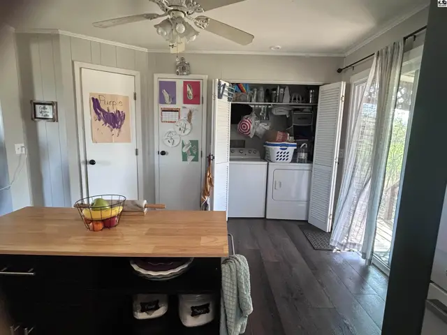 Kitchen island with butcher block top faces laundry area with white washer and dryer, and paneled walls.