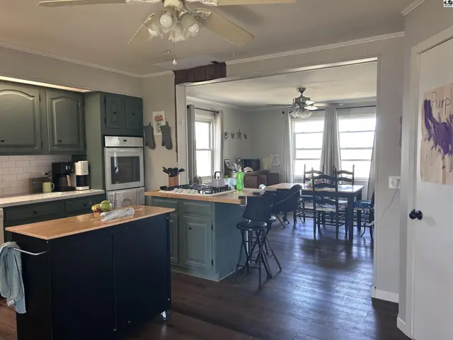 Spacious kitchen with dark green cabinets and island opens to a dining area with hardwood floors.