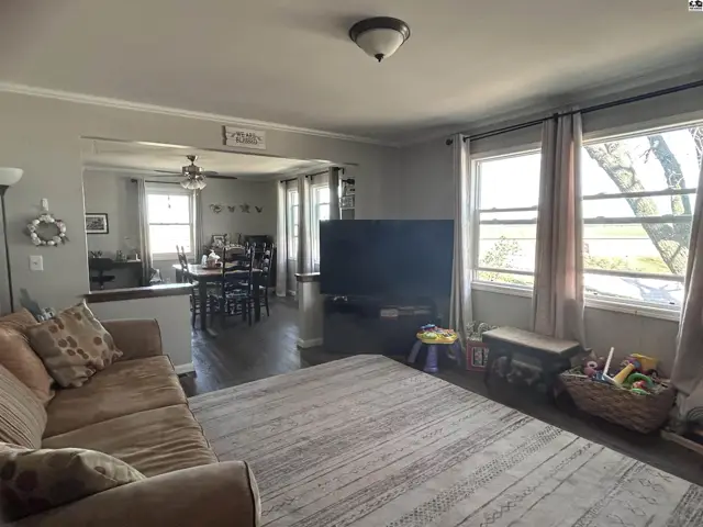 Spacious living room with a large TV and dining area, featuring hardwood floors and neutral tones.