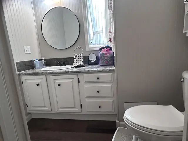 Bright bathroom with white vanity, granite countertop, round mirror, and a white toilet.