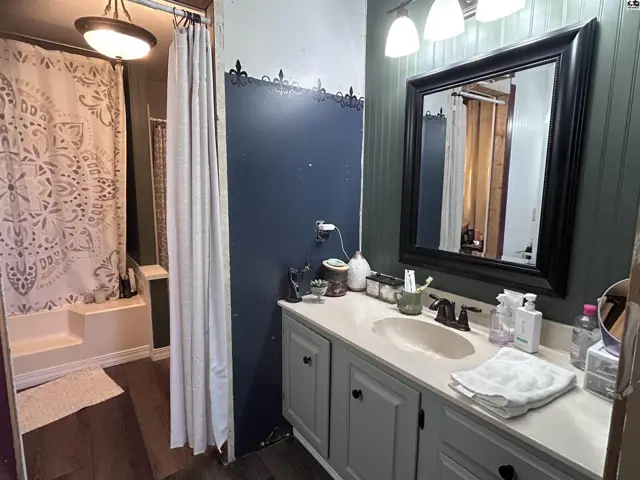 Bathroom with gray vanity, white countertop, dark framed mirror, and a tub/shower with a patterned curtain.