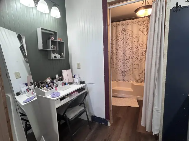 Vanity area with makeup and a view into a bathroom with a patterned shower curtain.