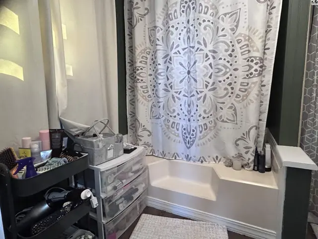 A bathroom features a white tub with a decorative shower curtain and organized storage.