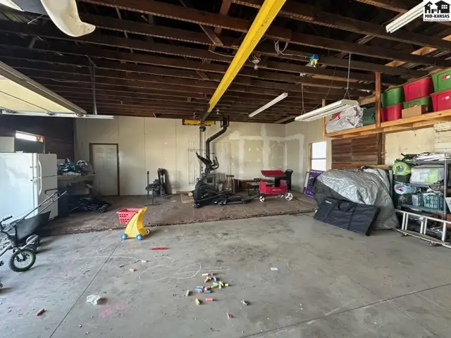Spacious garage with unfinished walls, exposed beams, and concrete floor, containing exercise equipment and storage.