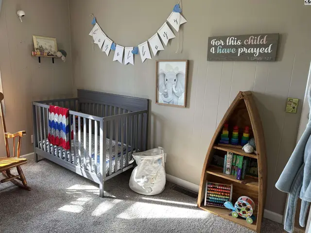 Nursery with gray crib, elephant art, and a unique wooden boat bookshelf.