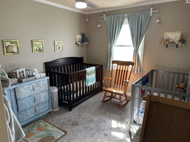 Nursery with two cribs, a blue dresser, and a rocking chair under a window with blue curtains.