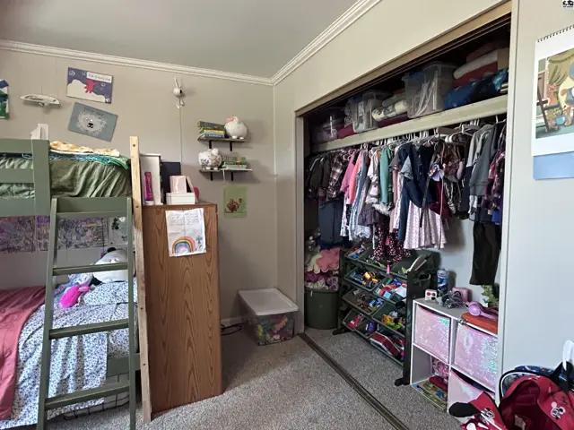 Children's bedroom with bunk beds, a wooden dresser, and a spacious closet filled with clothes.