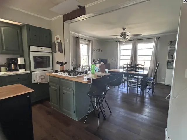 Open-concept kitchen with green cabinets and island, flowing into a dining area with dark wood floors.