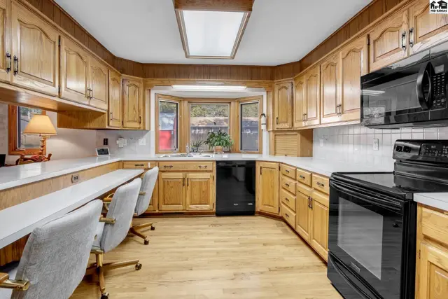 Spacious kitchen with light wood cabinets, white countertops, black appliances, and a bay window.