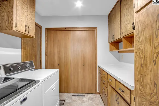 Laundry room with white appliances, light wood cabinets, and a white countertop.