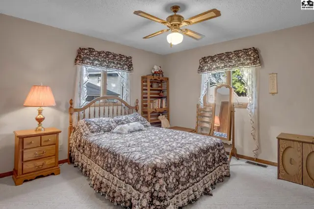 Cozy bedroom with a floral comforter, wooden furniture, and a ceiling fan.
