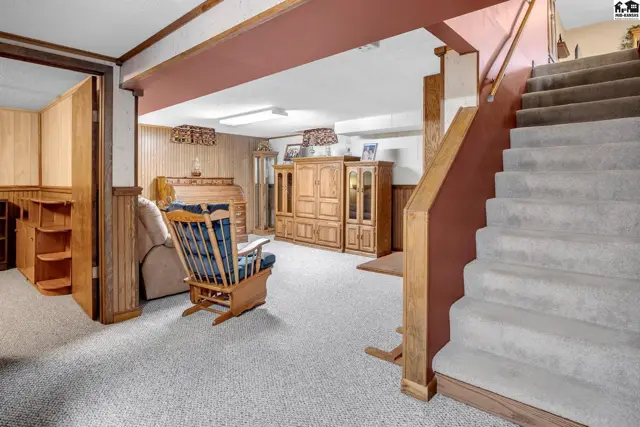 Cozy basement living area with wood paneling, plush carpet, and a carpeted staircase.