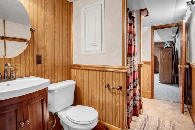 Bathroom with wood-paneled walls, white vanity, toilet, and a red and white shower curtain.