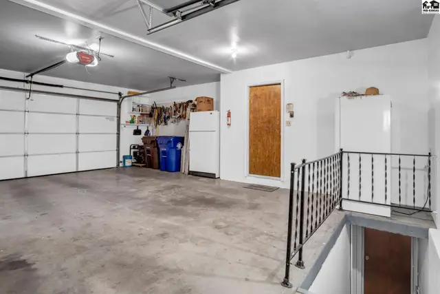 Spacious garage with two white doors, concrete floor, and a metal railing leading downstairs.