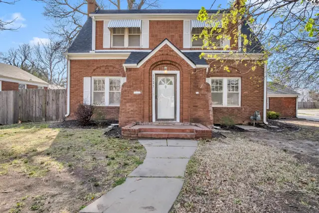 Brick two-story home with a charming arched entryway, white shutters, and a gambrel roof.