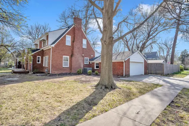 Brick home with a detached garage, large tree, and paved driveway on a sunny day.