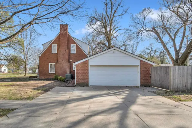 Brick house with attached garage, featuring a prominent chimney and mature trees.
