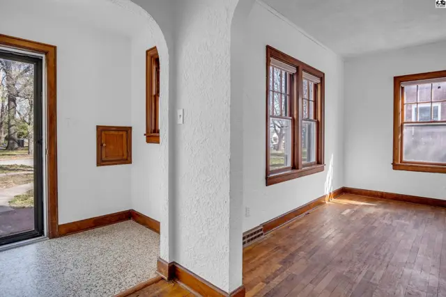 Interior view of a living room with hardwood floors, white textured walls, and warm wood trim.