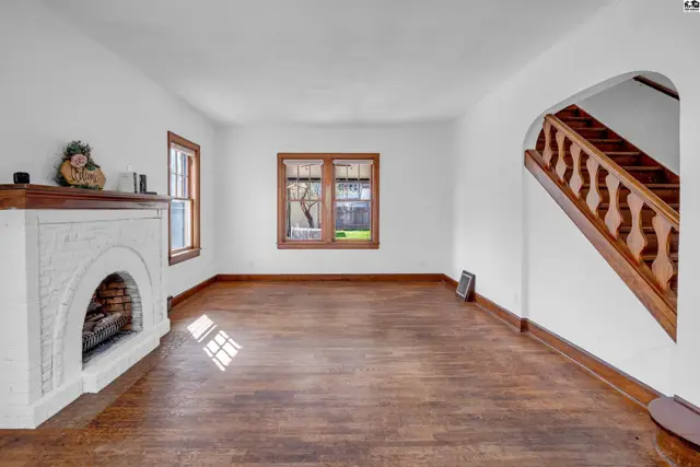 Living room with white brick fireplace, hardwood floors, and wooden staircase.