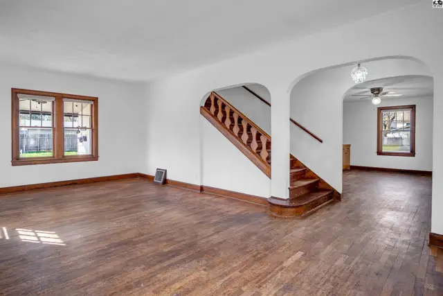 Spacious living room with hardwood floors, a prominent wooden staircase, and arched doorways.