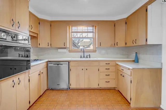 Bright kitchen with light wood cabinets, white countertops, stainless steel appliances, and tile flooring.
