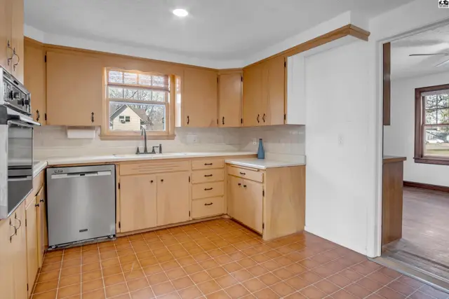 Kitchen with light wood cabinets, white countertops, stainless steel dishwasher, and tile flooring.