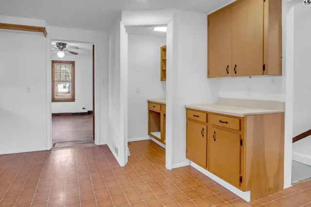 Kitchen area with wood cabinets and tile floor, opening to a living room with hardwood floors.