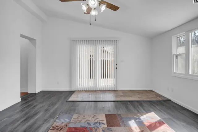 Spacious living room with vaulted ceiling, vertical blinds, and dark wood-look flooring.