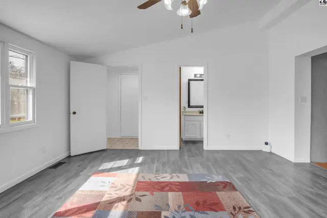Spacious bedroom with vaulted ceiling, gray wood-look flooring, and a colorful rug leading to a bathroom.
