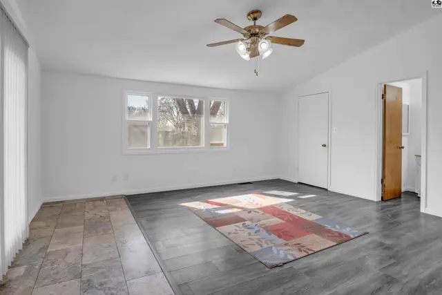 Spacious living room with white walls, wood-look flooring, tile accent, and a ceiling fan.