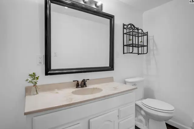 Bright bathroom with white vanity, beige countertop, black framed mirror, and toilet.