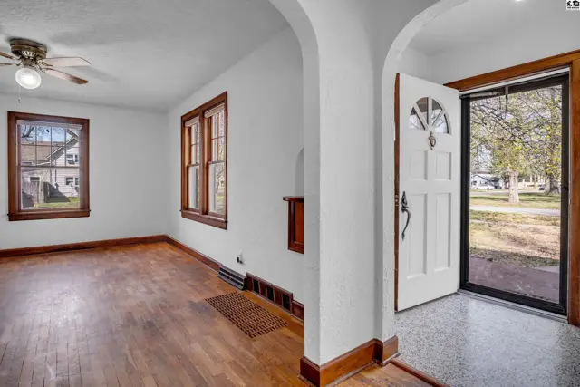 Bright entryway with white door and glass sidelight opens to a living room with hardwood floors and wood trim.