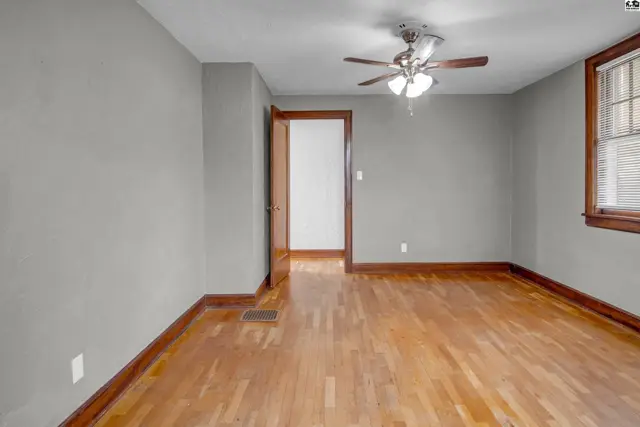Spacious room with gray walls, hardwood floors, ceiling fan, and a doorway to another room.