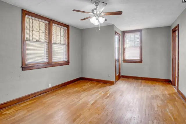 Spacious room with hardwood floors, gray walls, and large windows with wooden trim.
