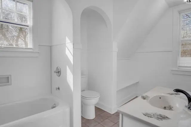 Bright white bathroom with a soaking tub, toilet, and vanity with a patterned countertop.