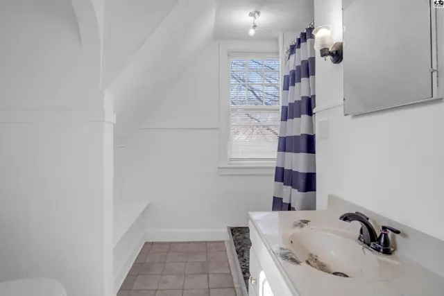 Bright bathroom with white vanity, tiled floor, and blue-striped shower curtain.